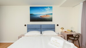 A hotel room with a bed, a desk, a chair, a lamp, and a painting of a beach. - Stunning home in Duba (Duba)
