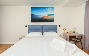 Ein Hotelzimmer mit Bett, Schreibtisch, Stuhl, Lampe und einem Strandbild.