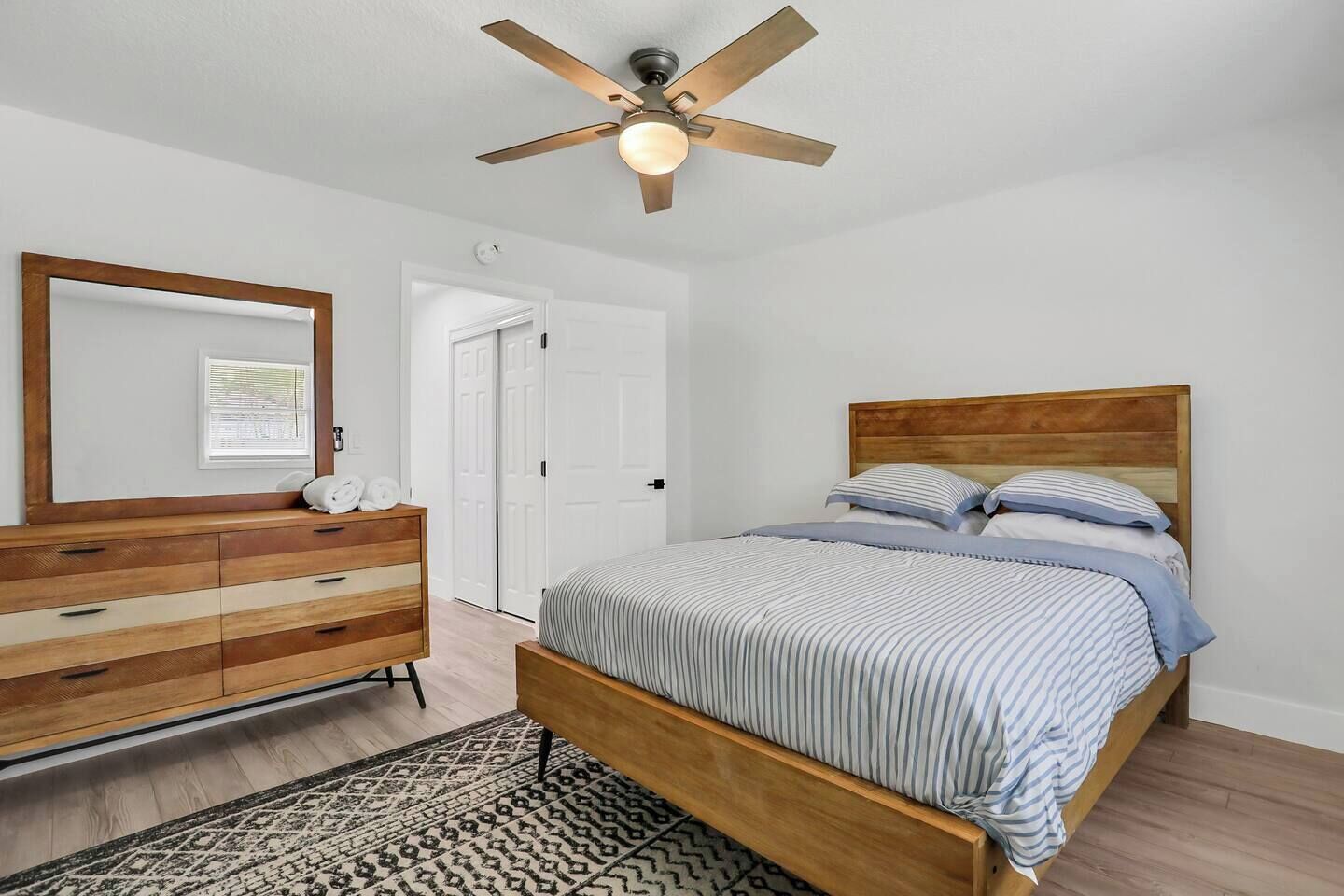 A bedroom with a wooden bed, a dresser, a ceiling fan, and a patterned rug.