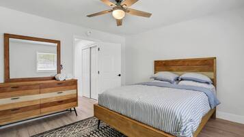 Een slaapkamer met een houten bed, een dressoir, een plafondventilator en een kamerbreed tapijt met een patroon.