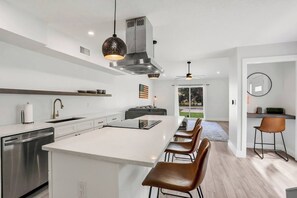 Eine moderne Küche mit Kochinsel, Edelstahlgeräten und einer Essecke mit Barhocker.