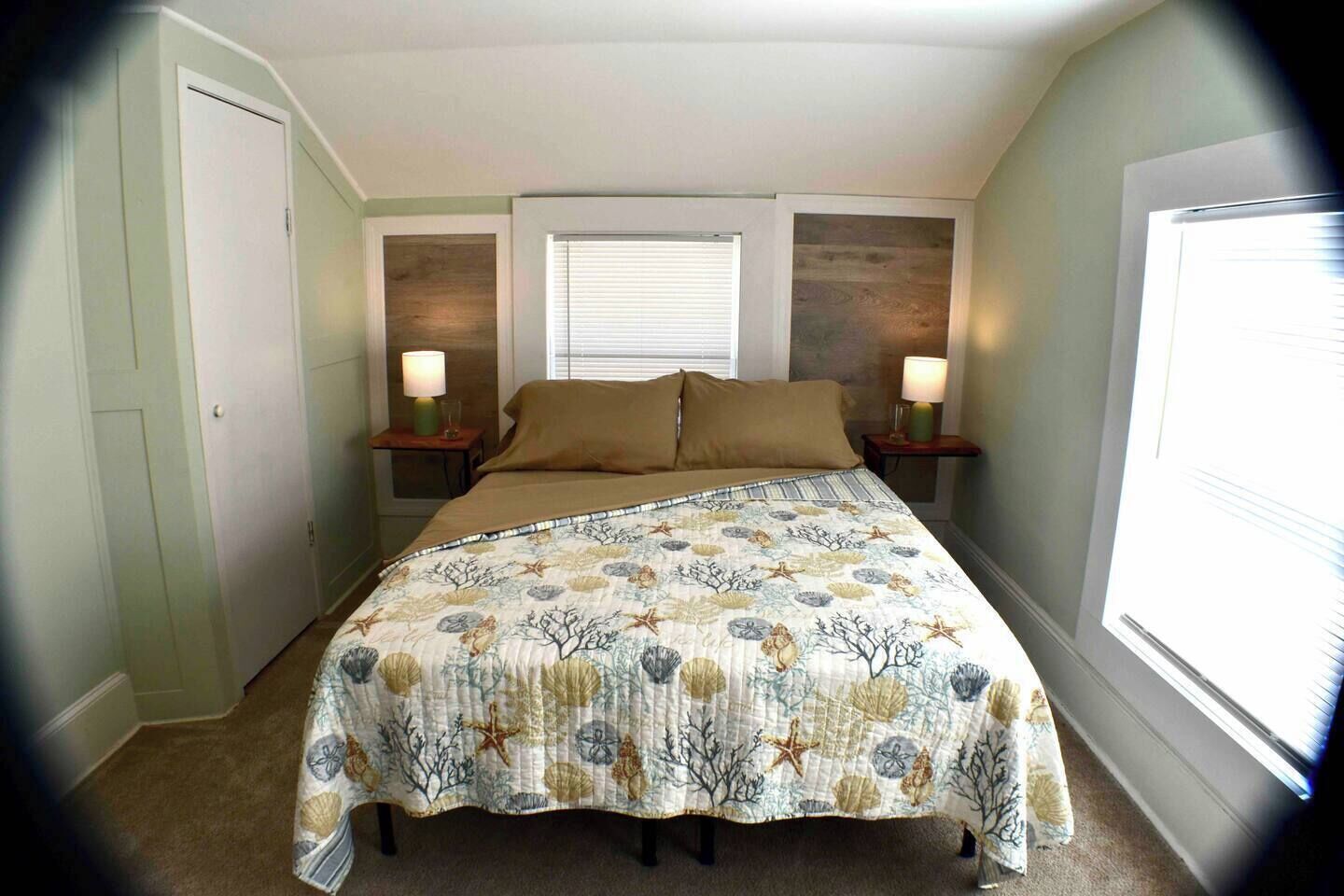 Un dormitorio con cama, dos mesitas de noche con lámparas, una ventana con persianas y una puerta.