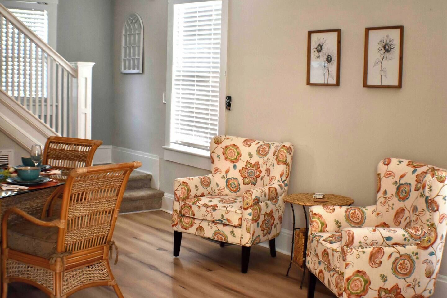Un comedor con sillas de mimbre, un sillón estampado con motivos florales y una pequeña mesita auxiliar.