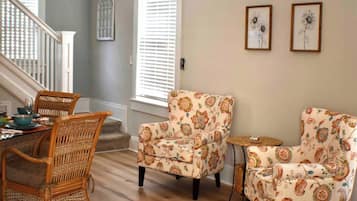 Un comedor con sillas de mimbre, un sillón estampado con motivos florales y una pequeña mesita auxiliar.