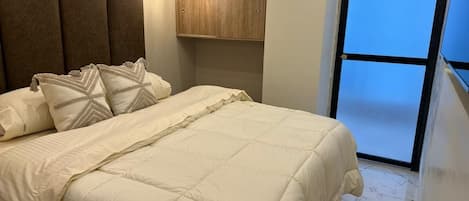 A bed with a quilted cover, a wooden headboard, and a wall-mounted light fixture.