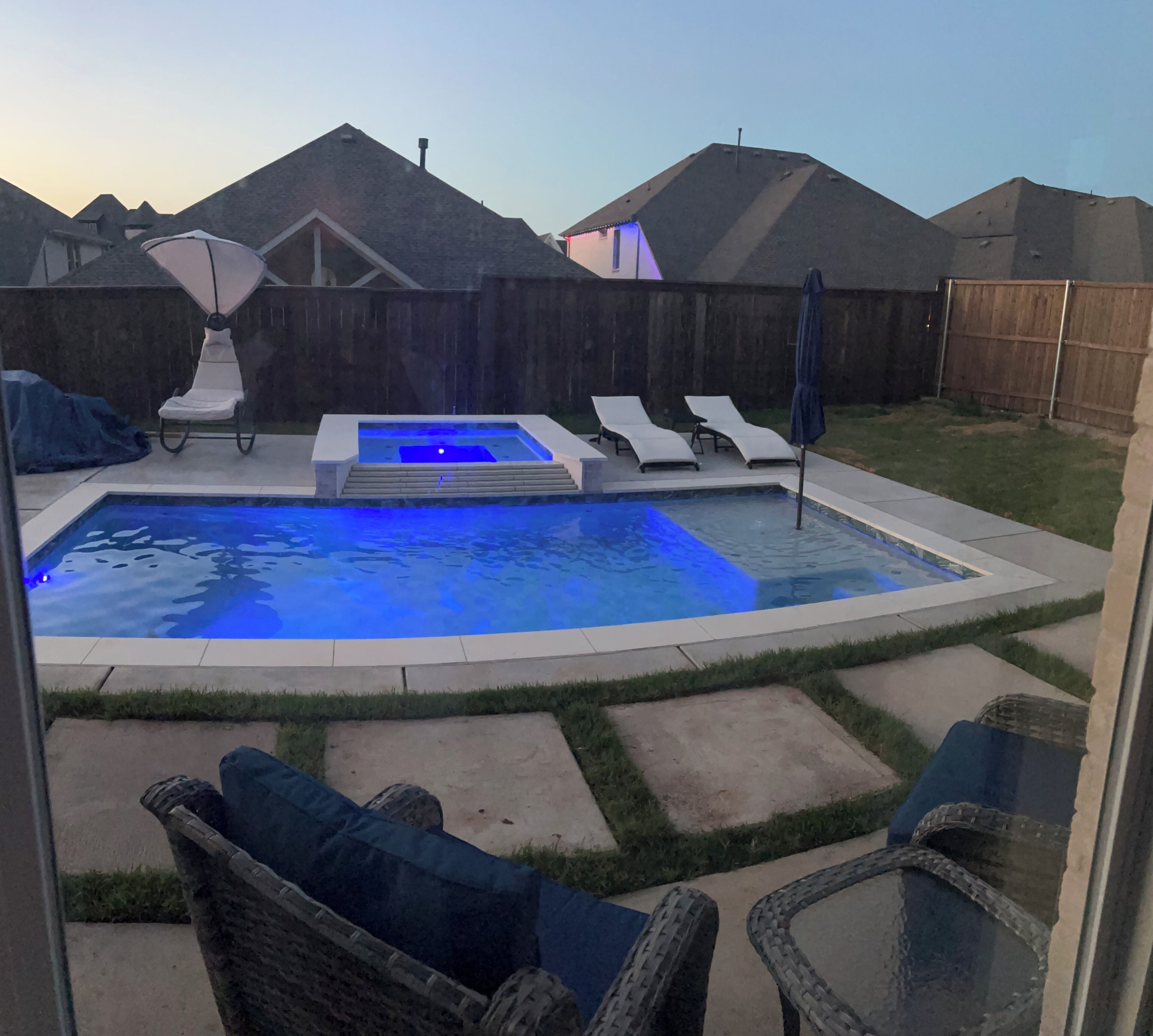 A backyard with a swimming pool, lounge chairs, and a hot tub.