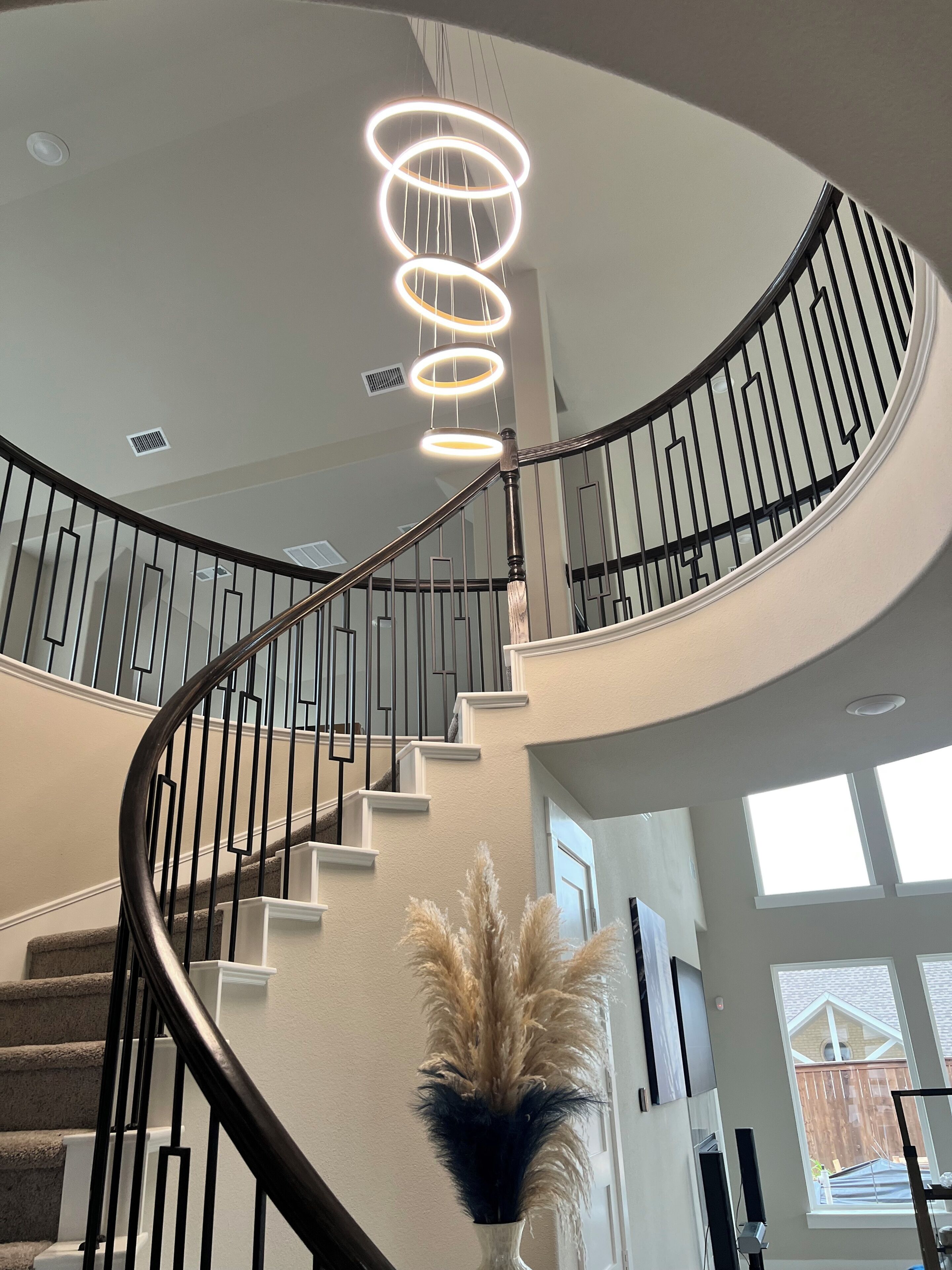 A spiral staircase with a modern design, a decorative vase with pampas grass, and a large window providing natural light.
