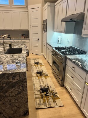 A modern kitchen with white cabinets, a stainless steel stove, and a marble countertop. - Huge 4 bdrm house in Fate with theater room, Pool table, & private pool/jacuzzi. (Rockwall)