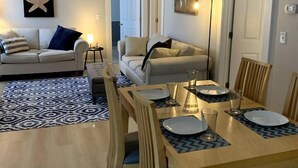 Ein Essbereich mit einem Holztisch, gedeckt für vier Personen, der von zwei Sofas und einem Teppich mit Muster eingerahmt wird.