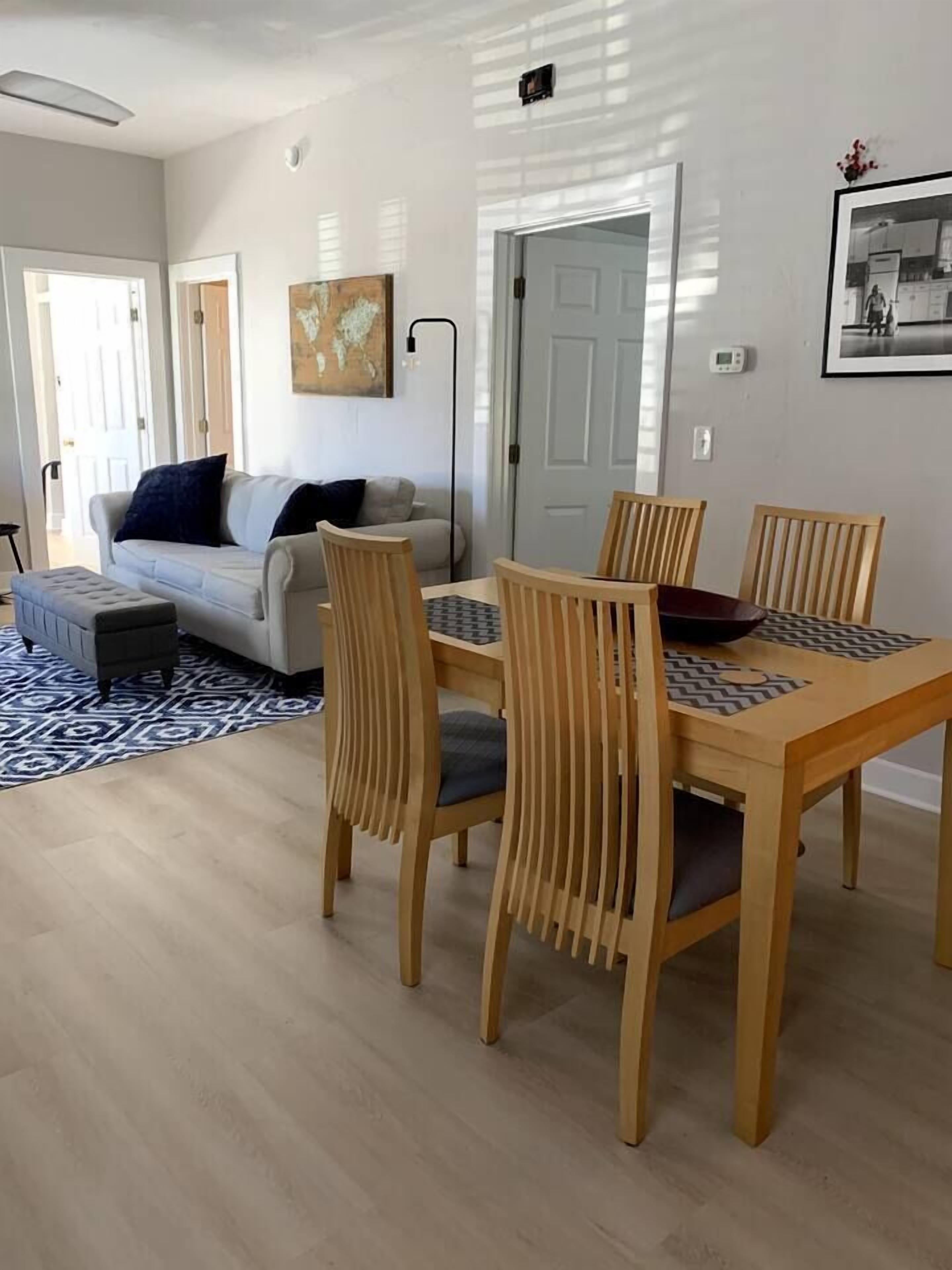 A dining area with a wooden table and chairs, a sofa, and a patterned rug.