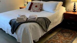 Ein ordentlich gemachtes Bett mit weißer Decke, Kissen und gefalteter Decke. Auf jeder Seite des Bettes stehen je eine Nachttischlampe.