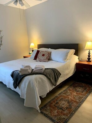 Ein ordentlich gemachtes Bett mit weißer Decke, Kissen und gefalteter Decke. Auf jeder Seite des Bettes stehen je eine Nachttischlampe.