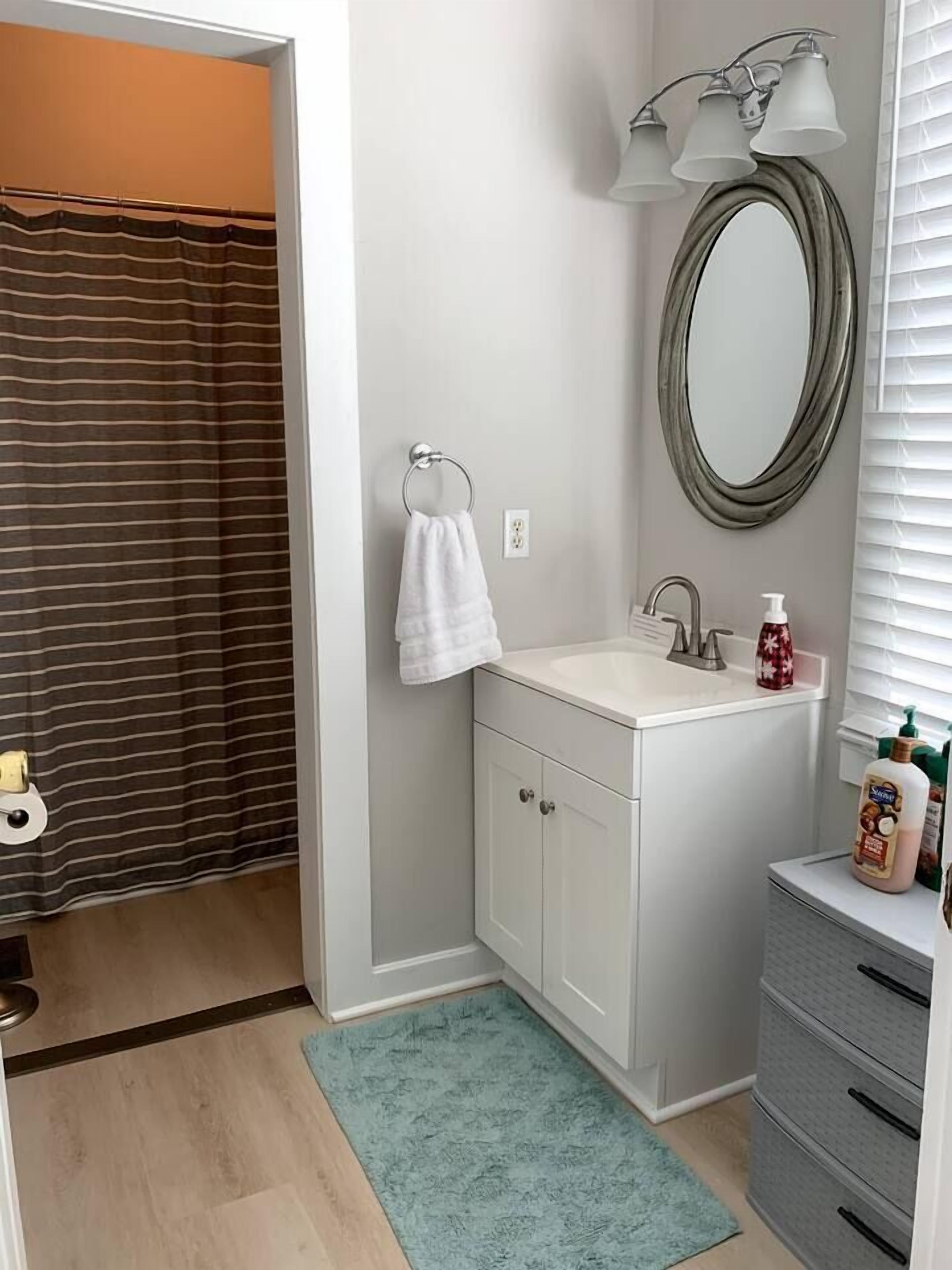 Ein Badezimmer mit Duschvorhang, Waschbecken mit Spiegel und Handtuchhalter.