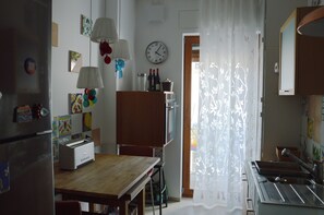 A kitchen with a wooden table, a refrigerator, a clock, and a window with a curtain. - Casa Fortu in centro. Luxury house with an alcove in the heart of Bari. (Bari)