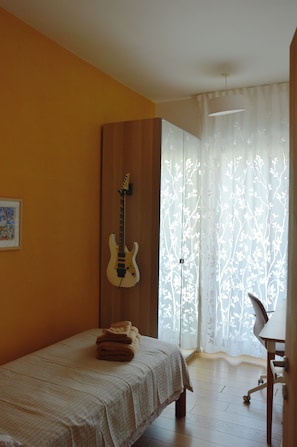 A bedroom with a bed, a guitar, a chair, and a window with curtains. - Casa Fortu in centro. Luxury house with an alcove in the heart of Bari. (Bari)