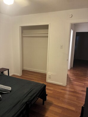 A bedroom with a bed, a nightstand, a closet, and a door leading to another room.