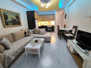 A living room with a sofa, a coffee table, a TV, and a dining area with chairs and a table.