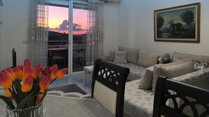 En stue med sofa, et billede og udsigt til en solnedgang gennem et vindue.