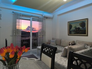 Ein Wohnzimmer mit einer Couch, einem Gemälde und Blick auf einen Sonnenuntergang durch ein Fenster.