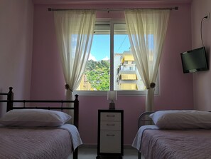 A bedroom with two beds, a TV mounted on the wall, and a window with curtains.