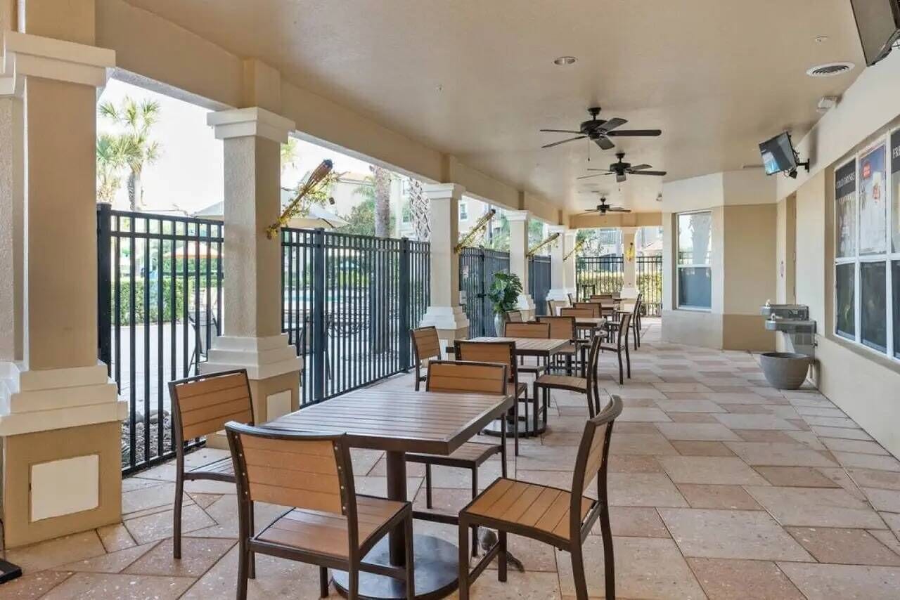 A covered outdoor dining area with multiple tables and chairs, a tiled floor, and ceiling fans.