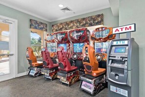 Une salle comprenant quatre bornes d’arcade proposant des jeux de course et un distributeur automatique de billets.