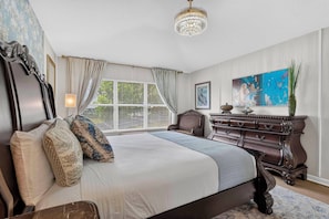 A bedroom with a large bed, a dresser, a chandelier, and a window with blinds. - WH2596 - 6BR House at Windsor Hills Resort (Kissimmee)