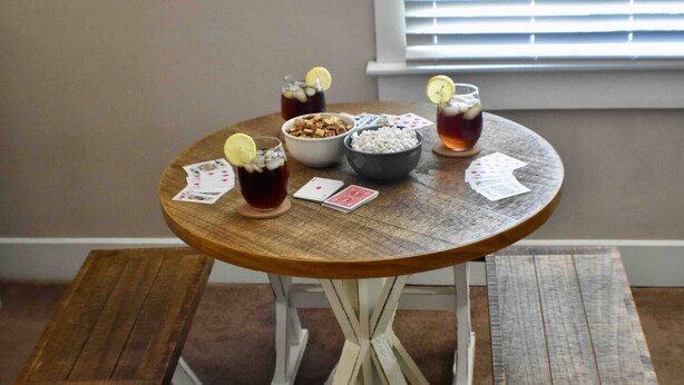 Una mesa redonda de madera con un cuenco de bocadillos, dos vasos de té helado con rodajas de limón y cartas.