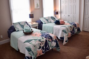 Una camera da letto con due letti, ognuno con copripiumino e cuscini a motivi floreali, un comodino con una lampada e un quadro appeso al muro.