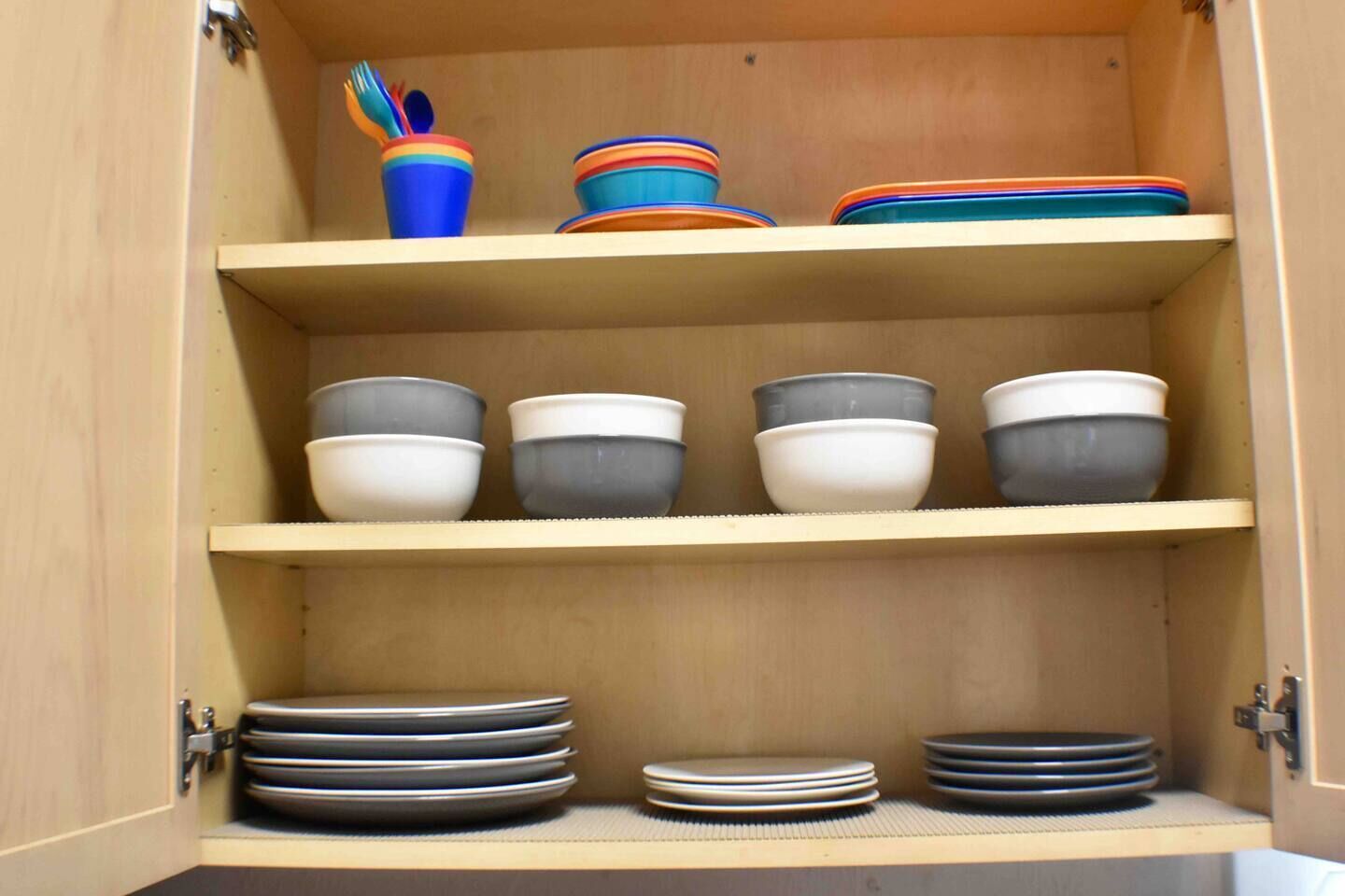 A wooden cabinet with three shelves, each holding bowls and plates.