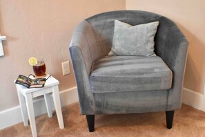 A grey armchair with a cushion, a small white side table with a drink and a menu, and a beige carpeted floor. - Cozy & Comfy 2/2 Apt ~ Walk to Historic Downtown (St. Augustine)