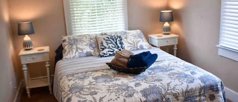 A bed with a floral bedspread, two bedside lamps, and a window with blinds.