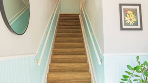 Una escalera con alfombra, barandilla, un espejo fijado a la pared y un cuadro con flores enmarco.