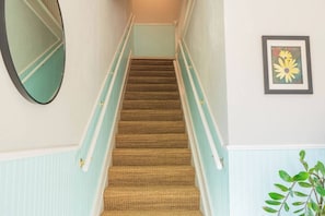A carpeted staircase with a handrail, a wall-mounted mirror, and a framed flower painting. - Cozy & Comfy 2/2 Apt ~ Walk to Historic Downtown (St. Augustine)