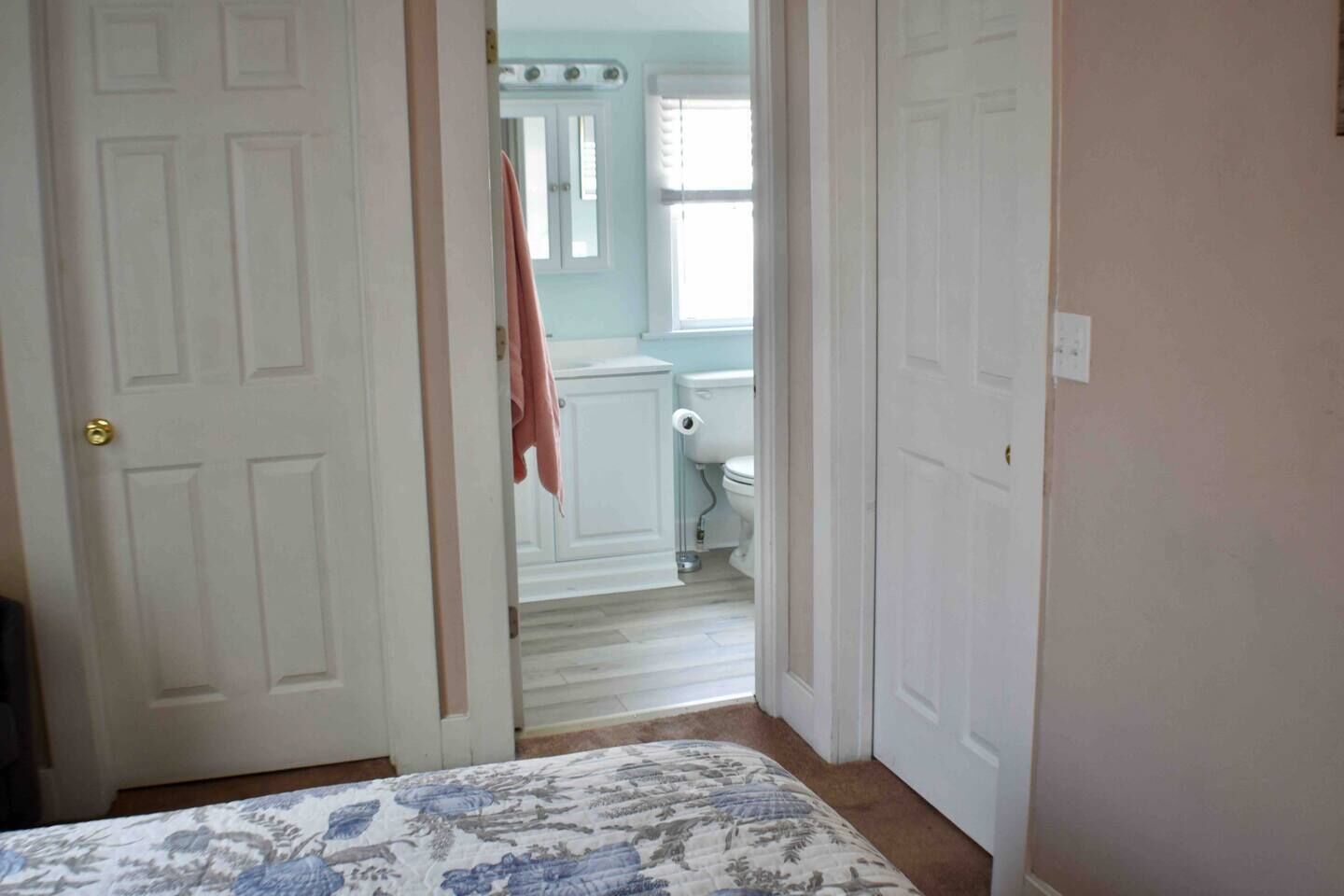 A bedroom with a bed, a bathroom with a toilet and sink, and a hallway leading to another room.