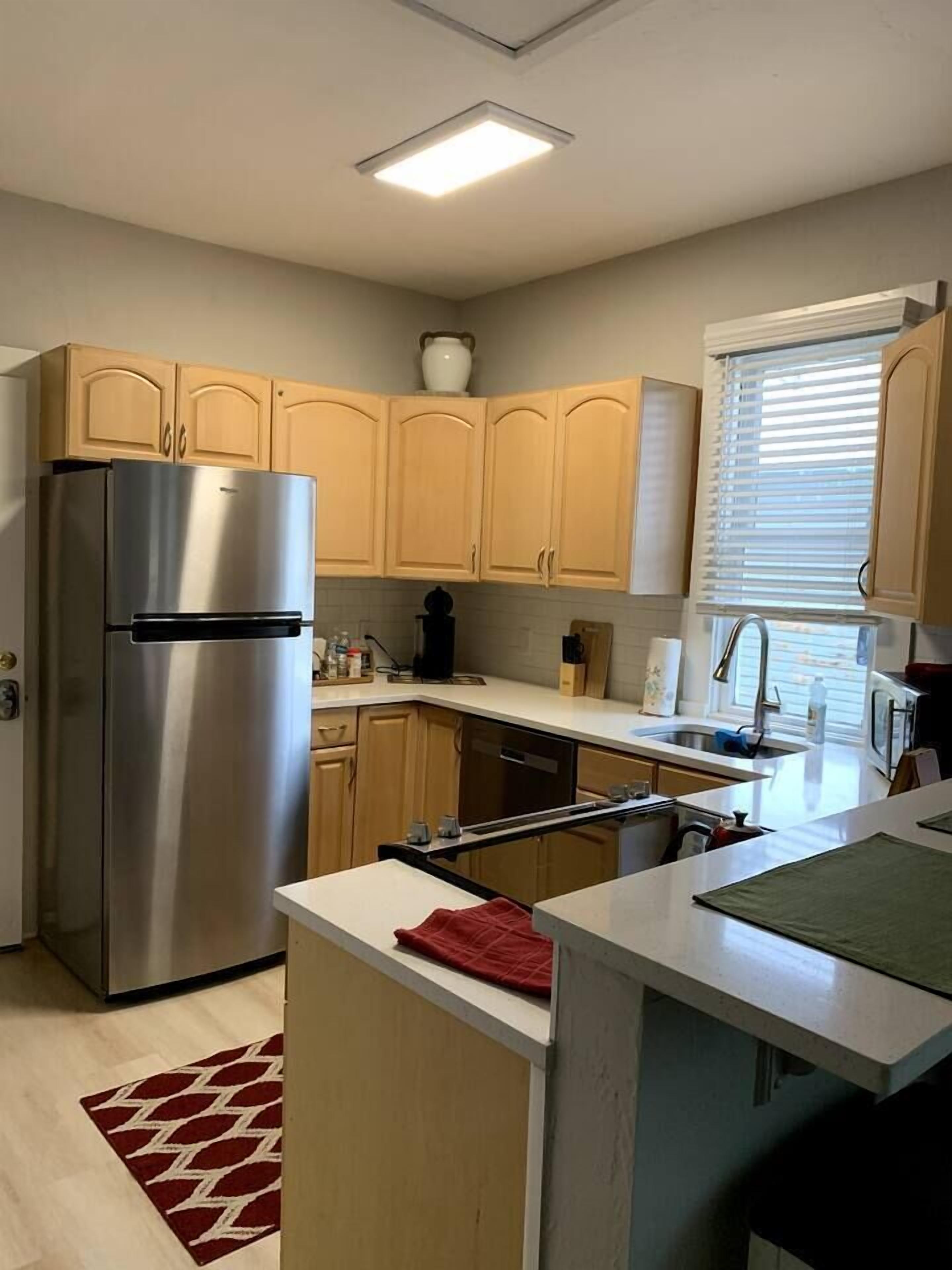 A modern kitchen with stainless steel appliances, wooden cabinets, and a window with blinds.