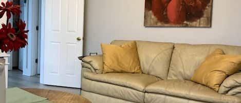 A living room with a beige sofa, a round wooden table, and a door leading to another room.
