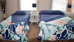 Una habitación con dos camas, cada una con una colcha estampada, una mesita de noche con una lámpara y un cuadro colgado en la pared.