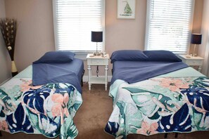 A room with two beds, each with a floral bedspread, a nightstand with a lamp, and a wall-mounted picture. - Cozy & Comfy 2/2 Apt ~ Walk to Historic Downtown (St. Augustine)