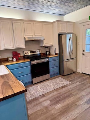 A kitchen with white cabinets, a stainless steel refrigerator, a stove, and a coffee maker. - Casa Carrera 2BR/2BA Main Cottage - Walk to Town (St. Augustine)