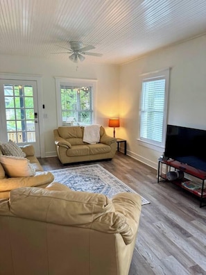 A living room with a beige sofa, a television, and a ceiling fan. - Casa Carrera 2BR/2BA Main Cottage - Walk to Town (St. Augustine)