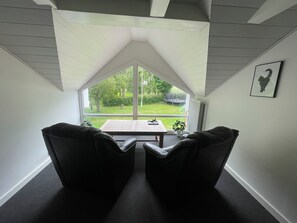 A room with a sloped ceiling, a large window, two black chairs, a small table, and a framed picture on the wall. - Lovely big house - quiet and beautiful - with garden and fence for dogs (Horslunde)