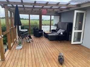 A covered outdoor patio with wooden flooring, seating arrangements, and a view of the countryside. - Lovely big house - quiet and beautiful - with garden and fence for dogs (Horslunde)