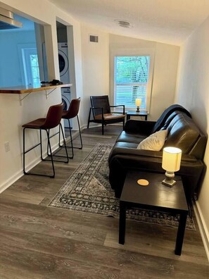 A compact living space with a sofa, two chairs, a small table, and a lamp. A washing machine is visible in the background. - 1BR/1BClean,CozyApt/Walk to town (St. Augustine)