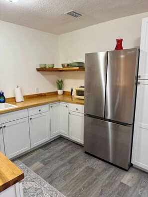 A compact kitchen with white cabinets, a stainless steel refrigerator, a wooden countertop, and a built-in microwave. - Casa Carrera 1BR/1BA Easy Walk to Town (St. Augustine)