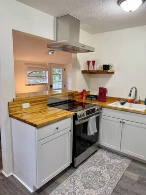 A compact kitchen with a built-in oven, a stovetop, and a sink. There is a window above the sink, and a small shelf with cups and a kettle. - 1BR/1BClean,CozyApt/Walk to town (St. Augustine)