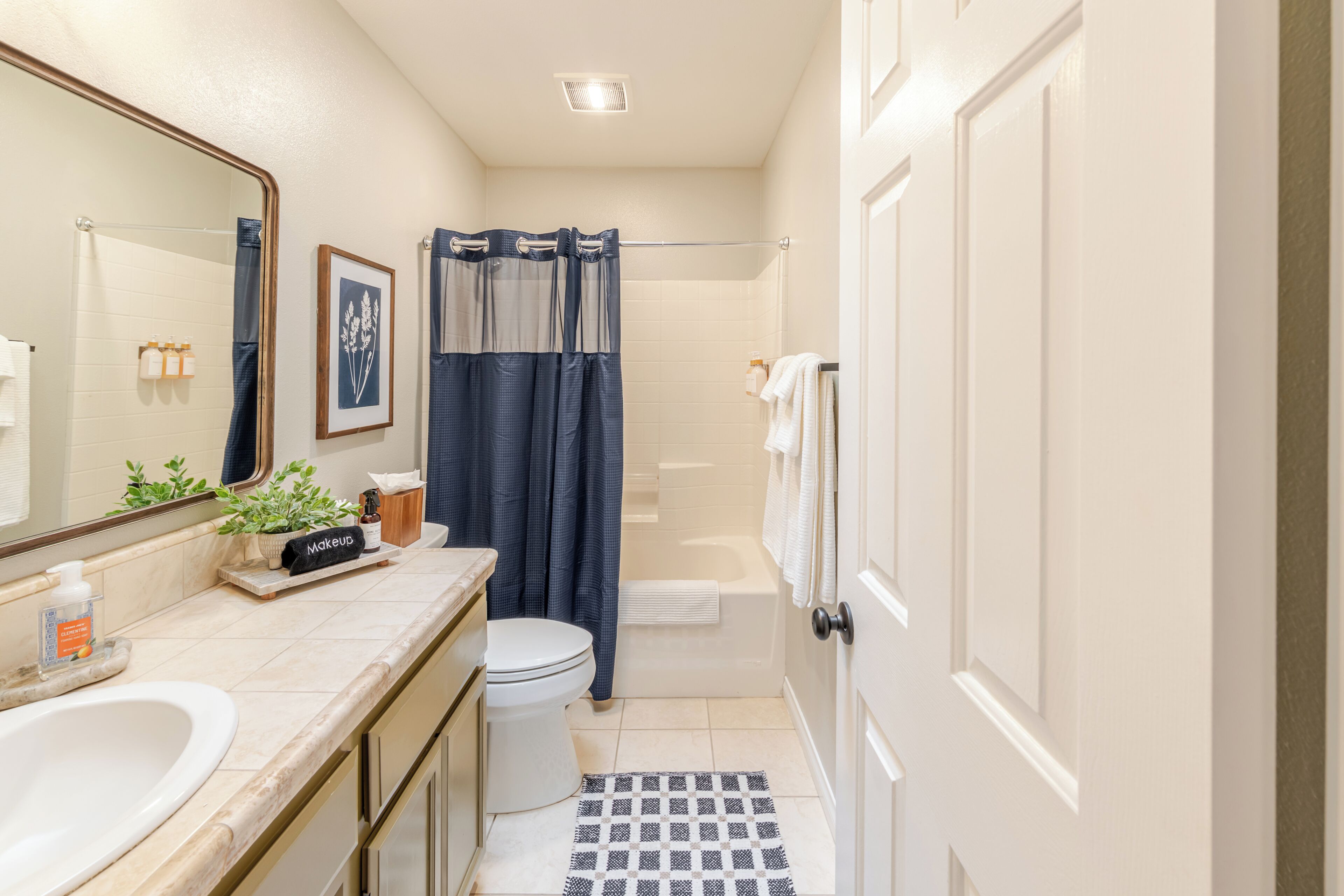 Une salle de bain équipée de toilettes, d’un lavabo, d’un miroir, d’un rideau de douche et d’une petite plante en pot.