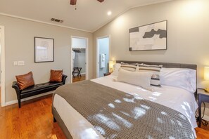 A bedroom with a large bed, a bench, a wardrobe, and a door leading to a bathroom.