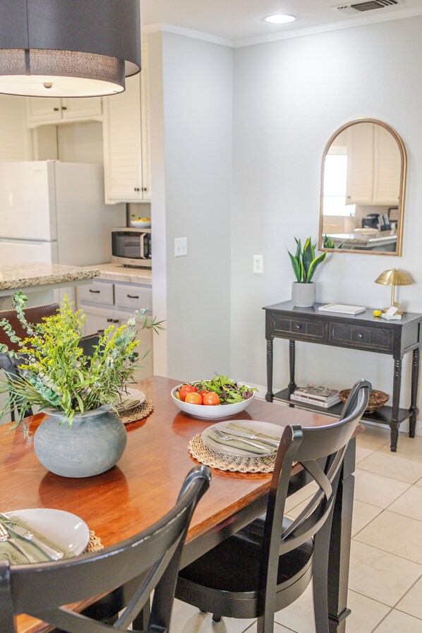 A dining area with a wooden table, chairs, a bowl of salad, and a potted plant.