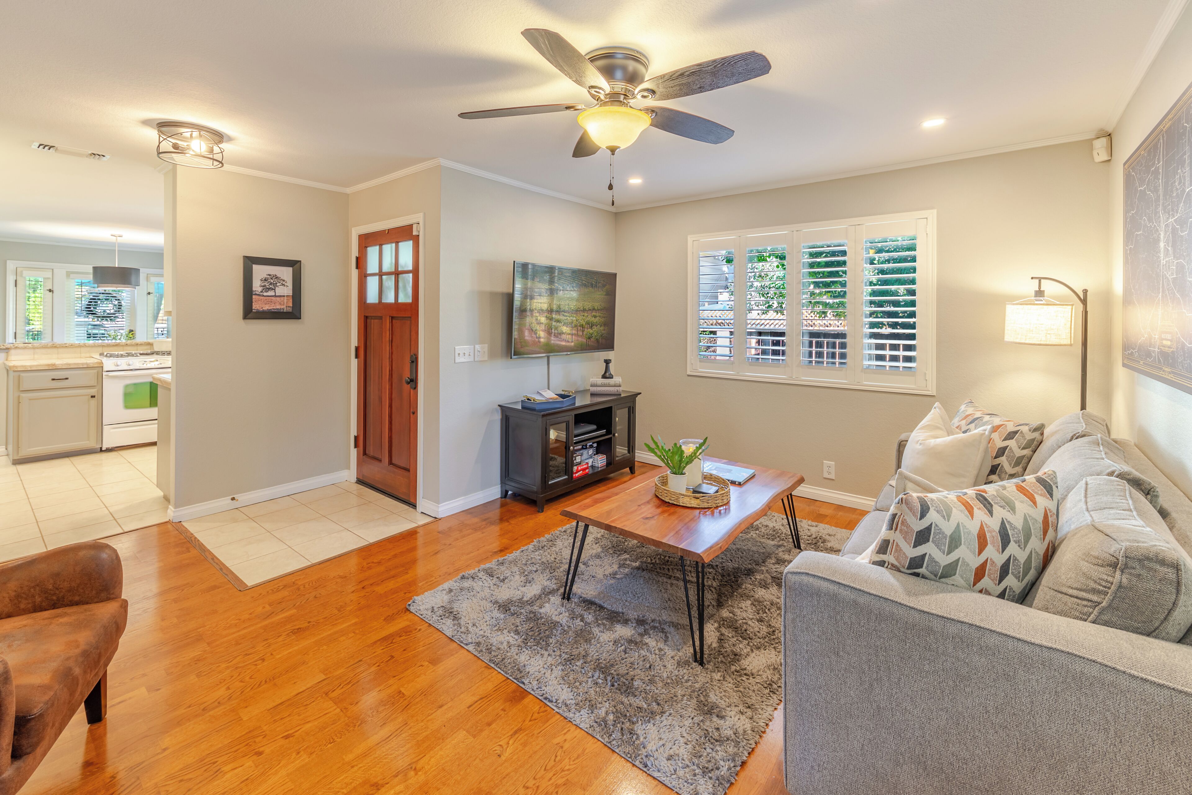 A living room with hardwood flooring, a ceiling fan, a television, a coffee table, and a sofa with patterned cushions.